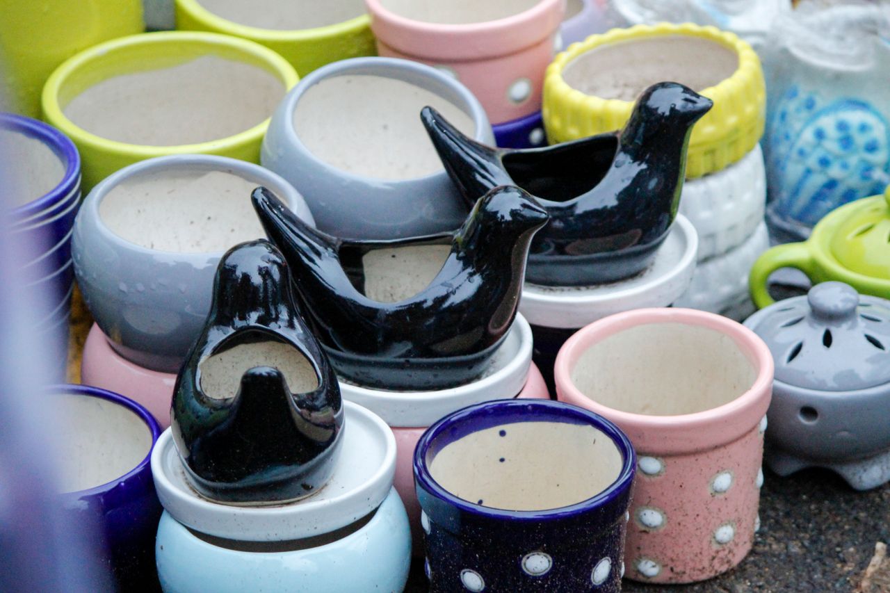 Home Assorted colorful ceramic pots and decorative bird sculptures on display at a market stall.