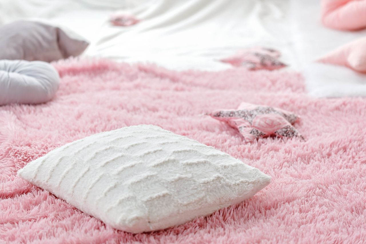 our-story Soft white pillow on a textured pink fluffy rug with blurred star decor. Perfect for cozy interiors.